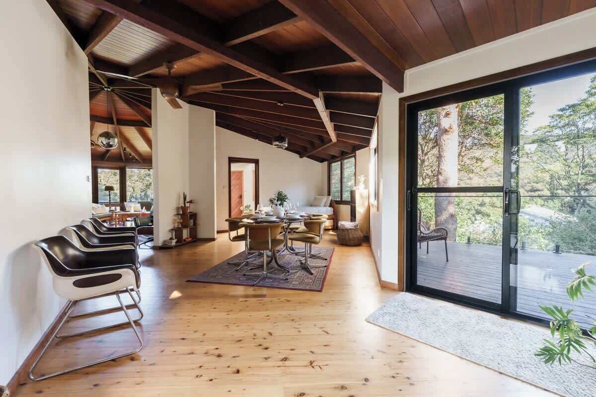 A spacious room with a wooden floor, a dining area with chairs and a table, and a large sliding glass door leading to an outdoor deck.
