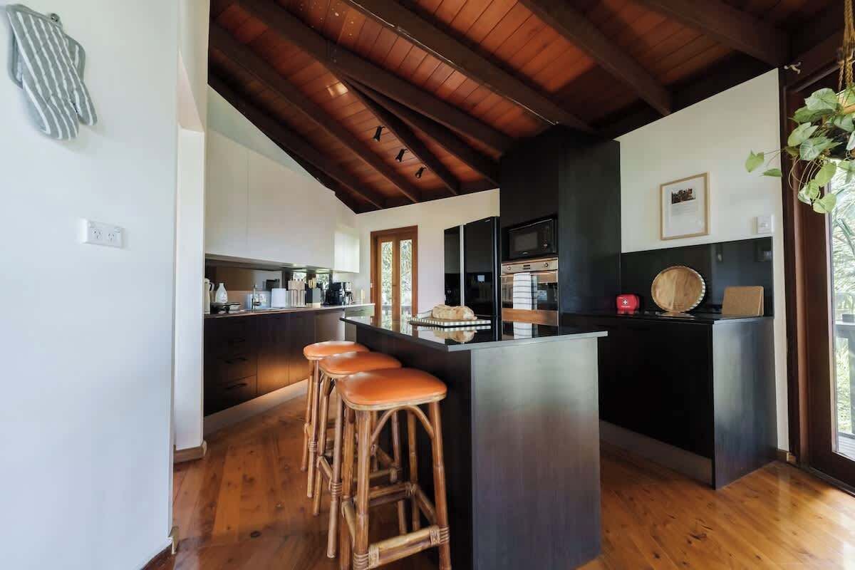 Una cocina moderna con una isla central, suelo de madera y un techo alto con vigas a la vista.