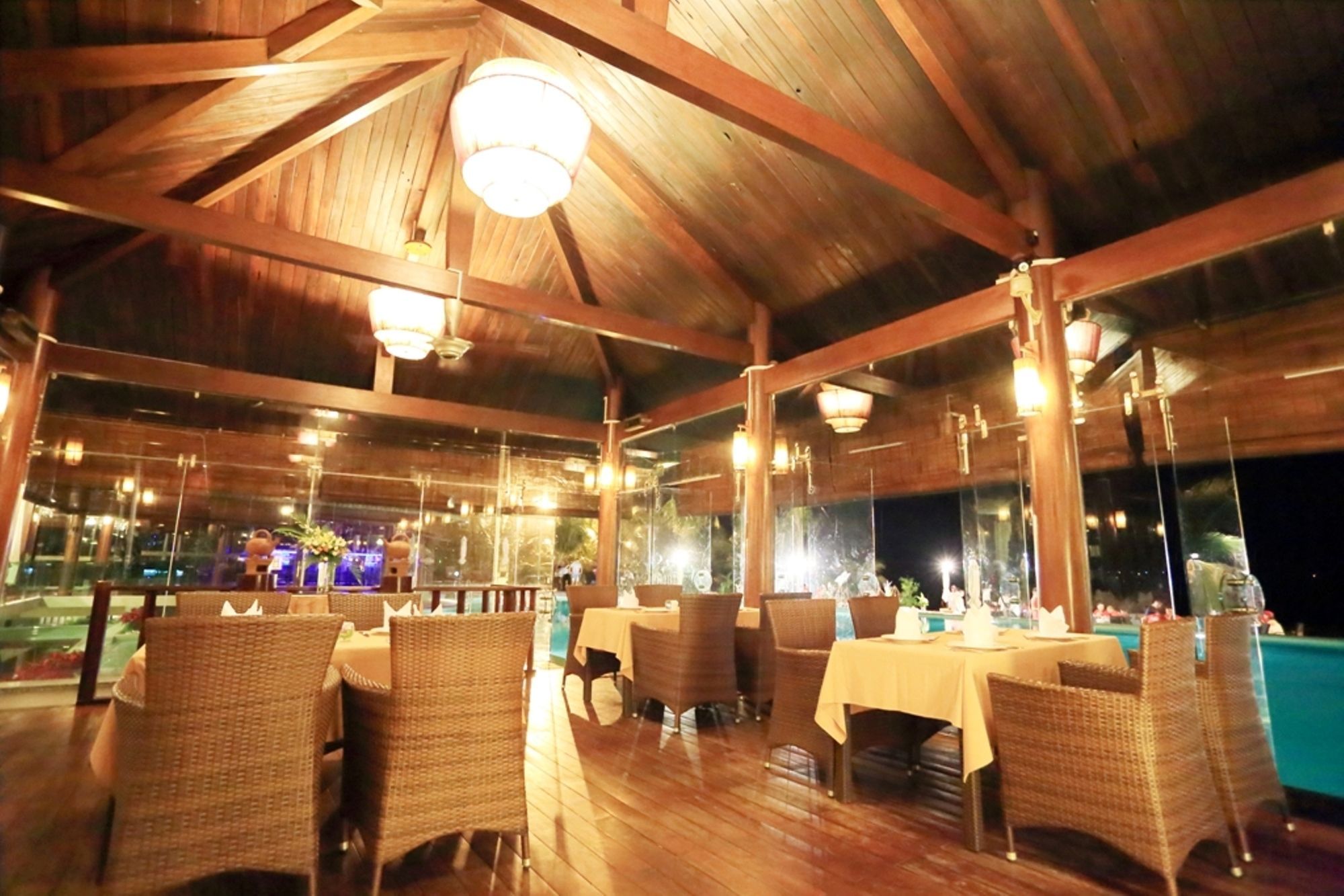 An indoor dining area with wooden beams, wicker furniture, and tables set for dining.