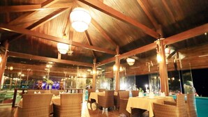 An indoor dining area with wooden beams, wicker furniture, and tables set for dining. - Villa Del Sol Beach Villas & Spa (Phan Thiet)