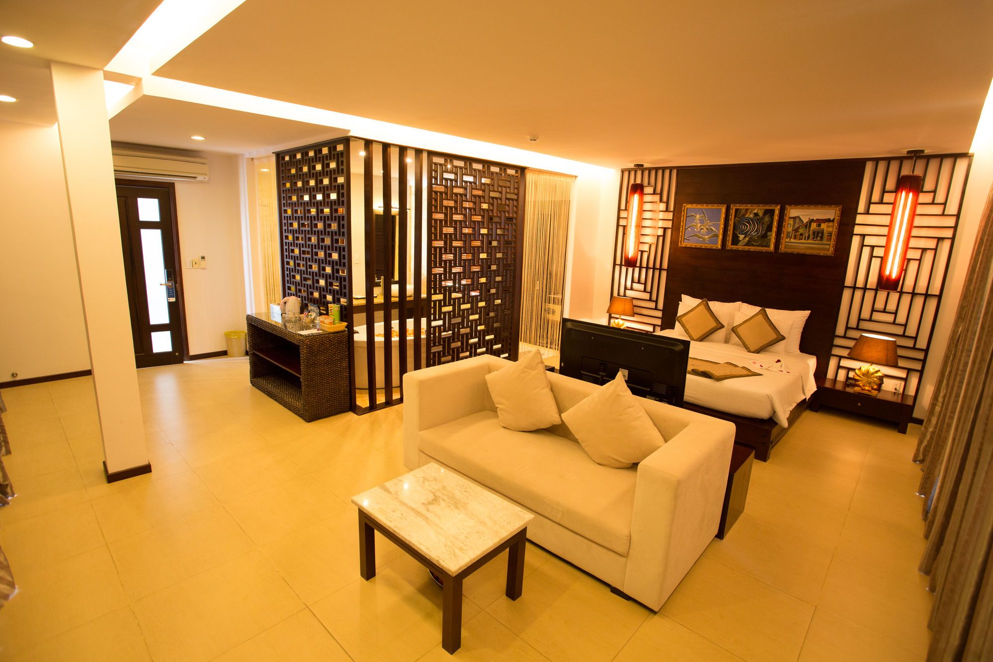 A hotel room with a sofa, a bed, a small table, and a decorative partition.