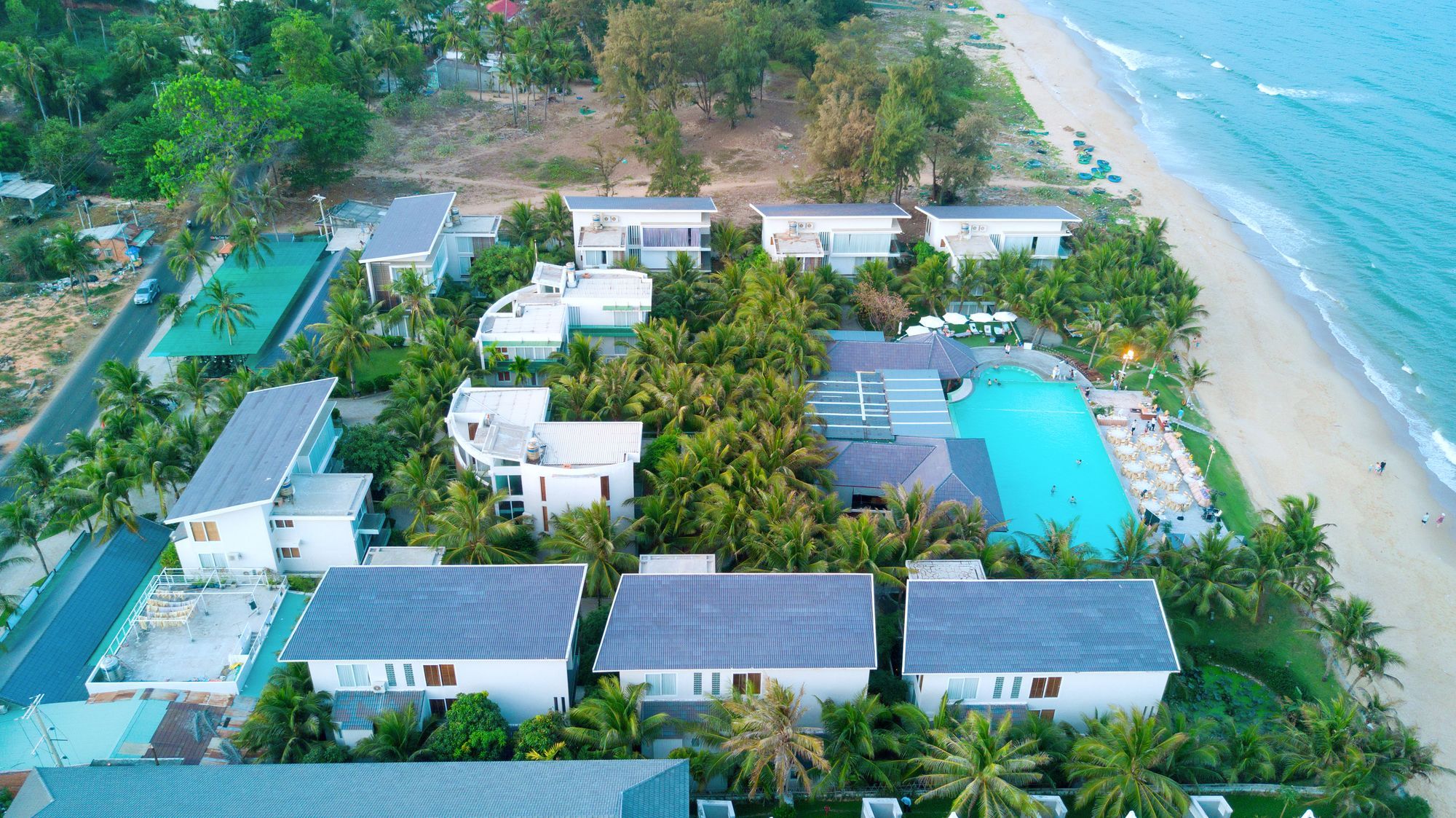 An aerial view of a resort with multiple buildings, a swimming pool, and a beach.