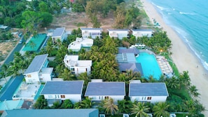 Ett flygbildsbild av ett semesterområde med flera byggnader, en swimmingpool och en strand.