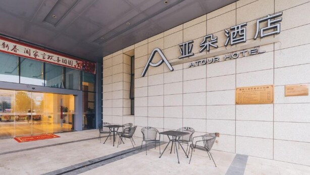 The exterior of the ATOUR HOTEL with a tiled facade, outdoor seating area, and a visible entrance. - Atour Hotel (Taizhou)