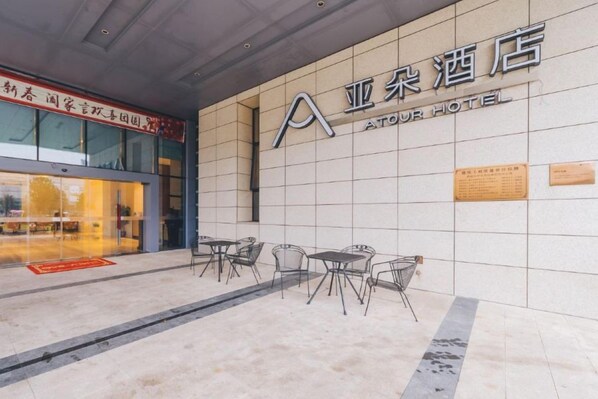 The exterior of the ATOUR HOTEL with a tiled facade, outdoor seating area, and a visible entrance. - Atour Hotel (Taizhou)