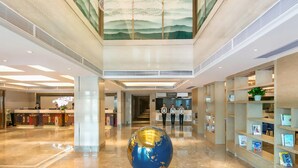 Un vestíbulo de hotel con un mostrador de recepción, una escultura de un globo terráqueo y una escalera que sube a los pisos superiores.