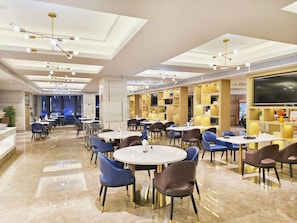 A modern dining area with round tables and chairs, a large TV screen, and a ceiling with recessed lighting. - Kyriad Marvelous Hotel Shenzhen Liuyue Metro Station (Shenzhen)