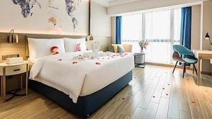 Habitación de hotel con una cama grande, un escritorio, una silla, un mapa mundial en la pared y vistas al exterior.