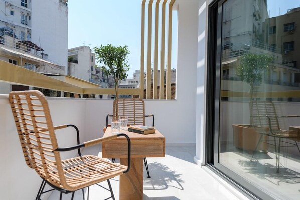A balcony with wicker chairs, a wooden table, and a glass partition.