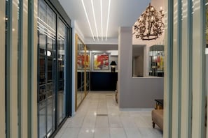 A hallway with a glass door, a chandelier, and framed artwork on the wall.