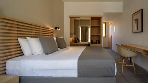 A hotel room with a bed, bedside table, chair, desk, wardrobe, and a mirror.