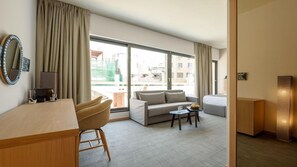 A hotel room with a desk, a sofa, a small table, and a bed. There is a large window providing a view of the outside. - Fos Hotel (Athens)