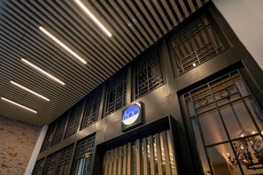 A building with a modern facade, a sign with the logo 'dba,' and a series of vertical light fixtures on the ceiling. - Fos Hotel (Athens)