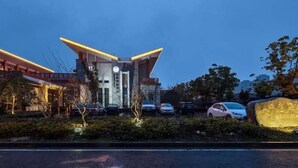 Een modern hotel met een opvallende ingang, een parkeerplaats en een grote rots met tekst erop.