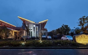 A modern hotel with a prominent entrance, a parking lot, and a large rock with text. - Begonia Hotel (Suzhou)