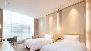 Een hotelkamer met twee bedden, een bureau, een stoel en een groot raam.