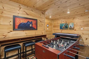 Una stanza con pavimento in legno, un tavolo da calcio e due sgabelli da bar.