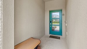 A narrow hallway with a teal door, a bench, and a welcome mat. - Pebble Beach Retreat (Kissimmee)