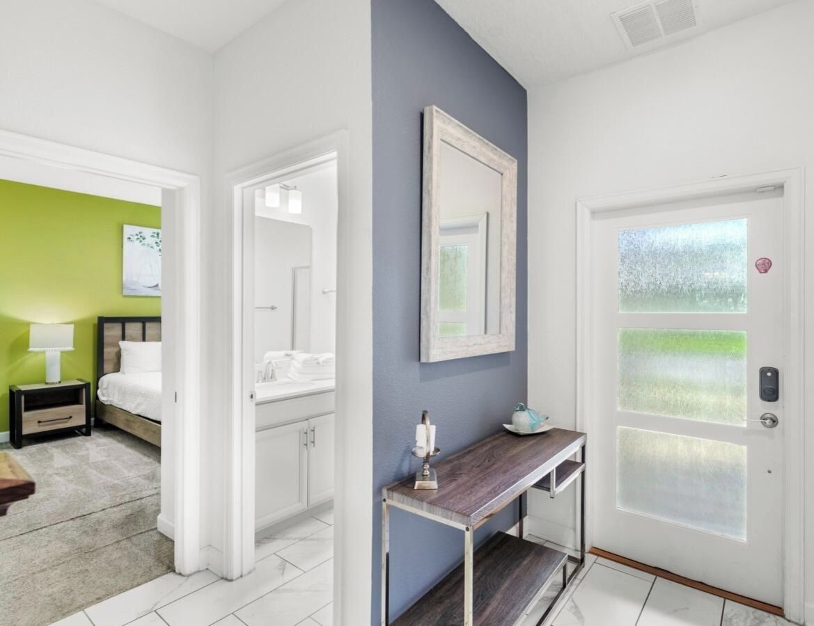 Une chambre d’hôtel comprenant un lit, une table de chevet, une commode, un miroir, une porte avec des panneaux en verre dépoli et une vue sur la verdure à l’extérieur.