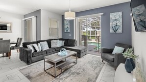 A modern living room with a sectional sofa, a coffee table, and a dining area with chairs. - Pebble Beach Retreat (Kissimmee)