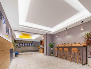 Un hall d’hôtel moderne doté d’un bar, de coins salon et d’une horloge décorative.