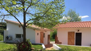 A white building with a red-tiled roof, a tree, and a wheelbarrow.