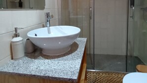 A bathroom with a white sink, a mirror, a shower enclosure, and a wooden vanity.