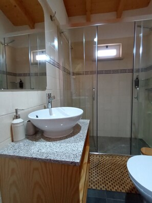 Un baño con lavamanos blanco, espejo, cabina de ducha y tocador de madera.
