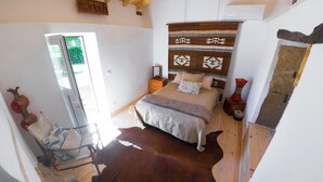 A bedroom with a bed, a wooden ceiling, a window, a chair, and a cowhide rug.