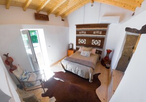Un dormitorio con cama, techo de madera, ventana, silla y alfombra de cuero de vaca.