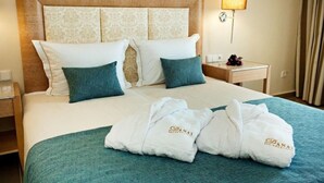 A hotel room with a large bed, two pillows, a nightstand, a lamp, and two towels with a logo. - Bomo Danai Hotel (Katerini)