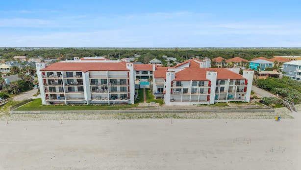 A multi-story hotel with balconies, a swimming pool, and a view of the surrounding landscape. - Las Brisas 523 (New Smyrna Beach)