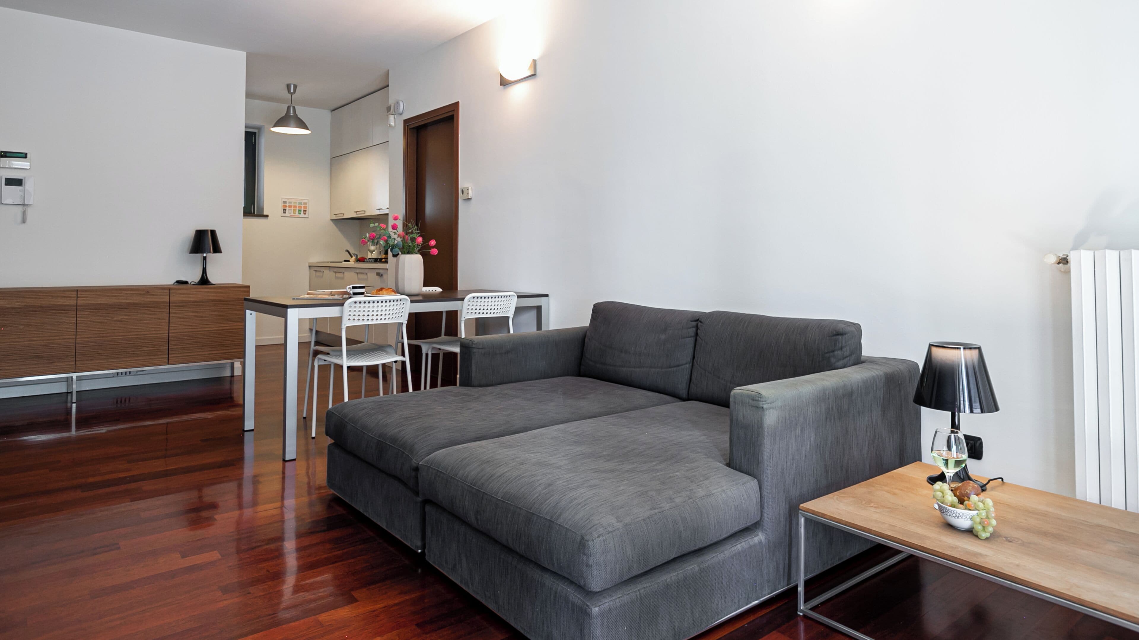 A modern living room with a grey sectional sofa, a wooden coffee table, and a dining area with white chairs.