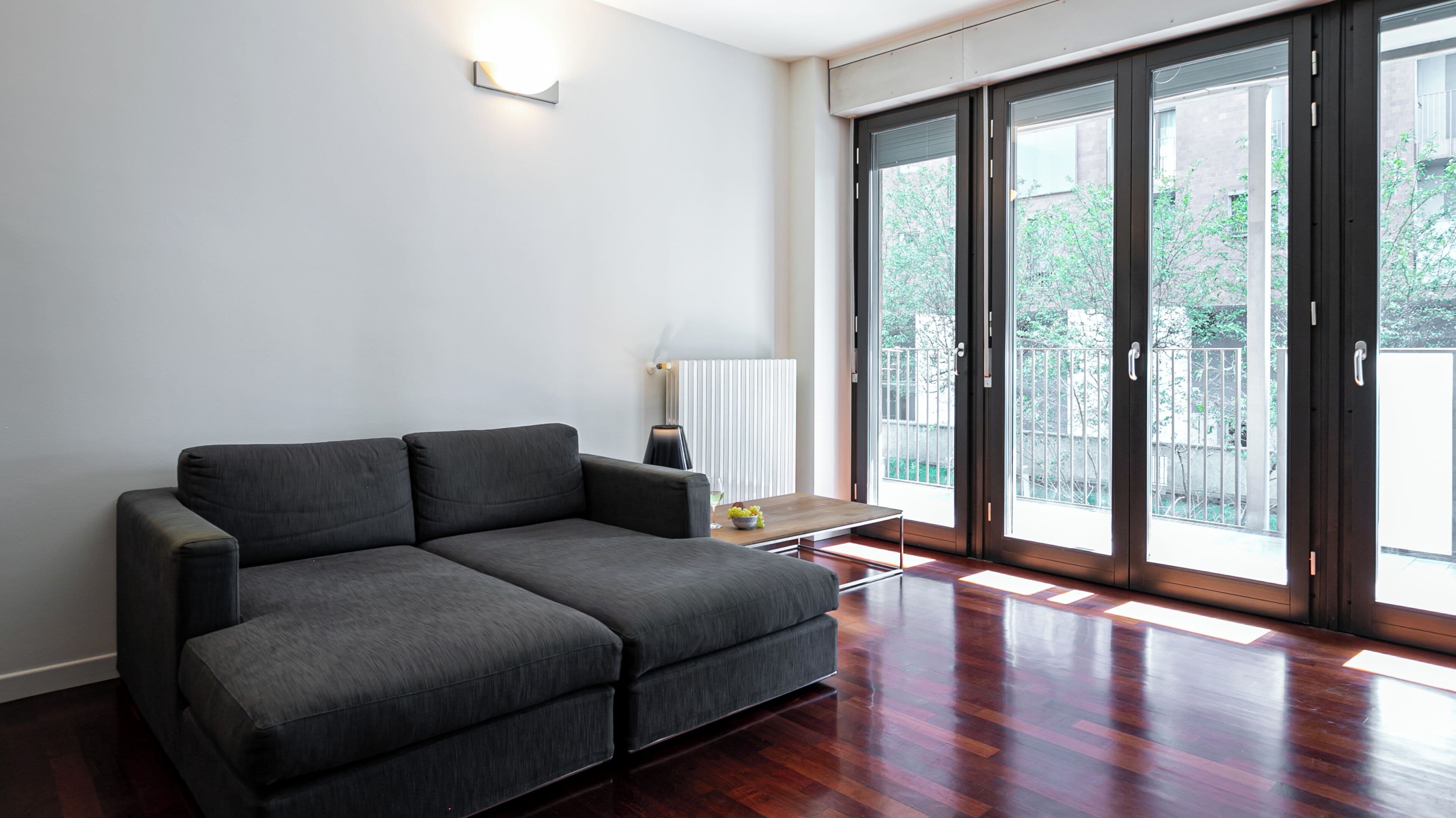 Un salon moderne avec un canapé gris, une petite table sur laquelle se trouve un saladier rempli de fruits, et un radiateur.