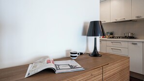 Uma cozinha com bancada de madeira, uma luminária preta, uma caneca e uma revista.