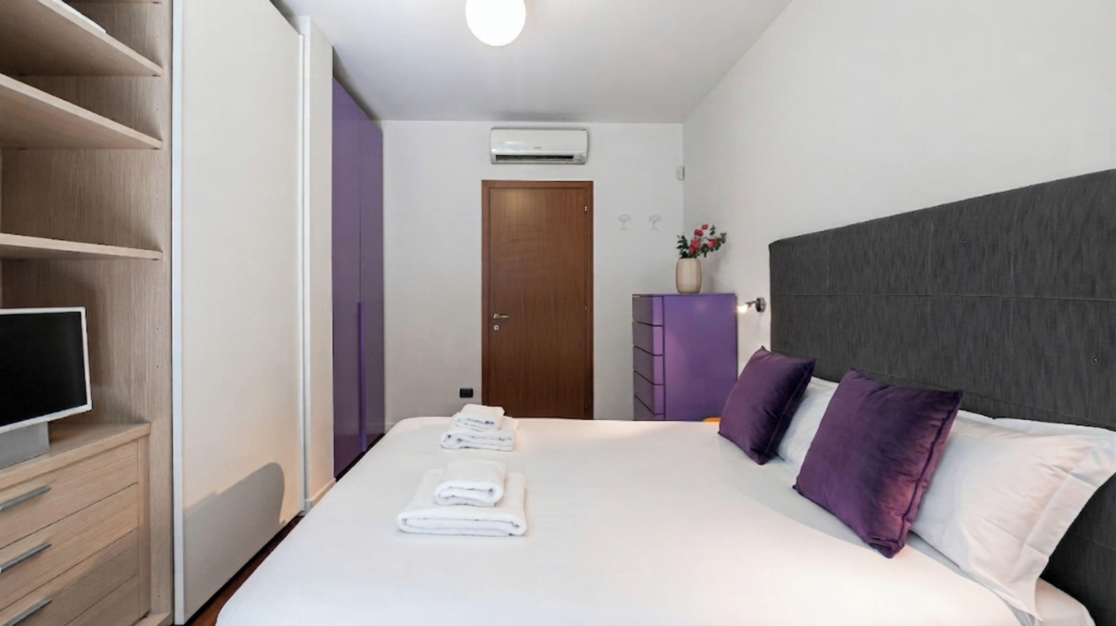 Hotellihuone, jossa on sänky, televisio, vaatekaappi ja ovi.