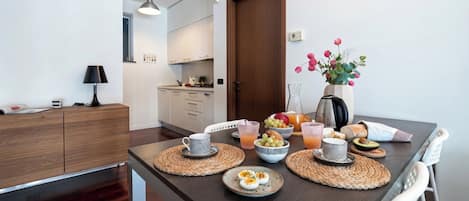 A modern kitchen with a dining table set for breakfast, including eggs, fruit, and beverages.