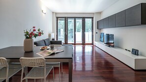 Uma sala de estar moderna com área de jantar, sofá, mesa de centro e TV em um armário branco.