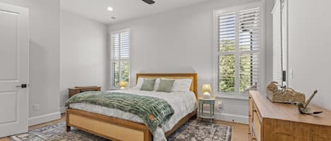A bedroom with a bed, bedside tables, a ceiling fan, and windows with blinds.