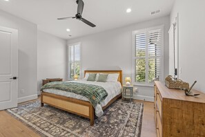 Ein Schlafzimmer mit einem Bett, Nachttischen, einem Deckenventilator und Fenstern mit Jalousien.