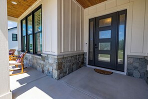 A house exterior with a stone foundation, a dark front door, and a porch with chairs. - Sweet Rose Cottage on Keowee with Beach Access (Seneca)