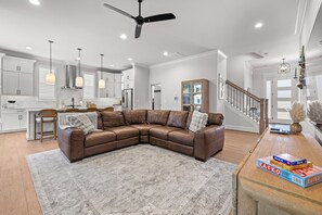A modern living room with a sectional sofa, a dining area with a kitchen in the background, and a staircase leading to another level. - Sweet Rose Cottage on Keowee with Beach Access (Seneca)