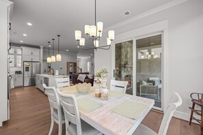 A modern kitchen with white cabinetry, a dining area with a wooden table, and a chandelier. - Sweet Rose Cottage on Keowee with Beach Access (Seneca)