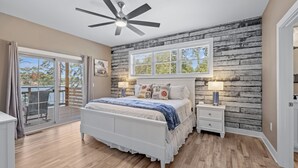 A bedroom with a bed, a nightstand, a ceiling fan, a window with blinds, and a view of a deck.