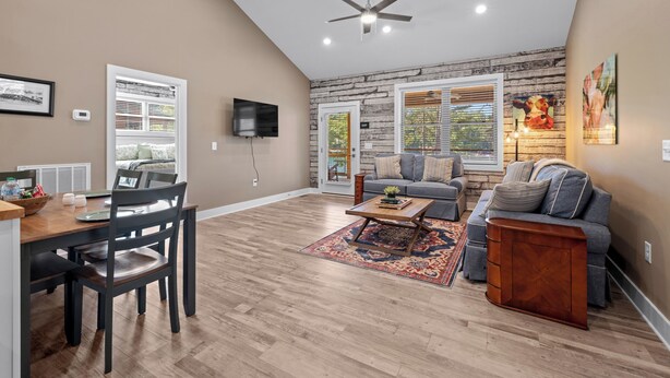 A spacious living room with a high ceiling, a ceiling fan, a large window, a fireplace, and a dining area with a table and chairs.