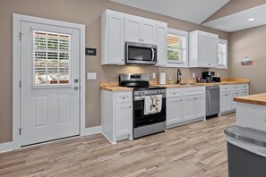 A modern kitchen with white cabinetry, a built-in oven, a microwave, and a coffee machine.