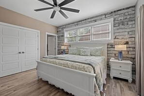 A bedroom with a bed, a nightstand, a ceiling fan, and a window with blinds.
