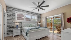 A bedroom with a bed, nightstands, a ceiling fan, a window with blinds, and a view of the outdoors.