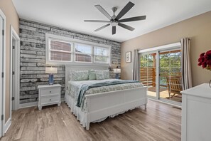 A bedroom with a bed, nightstands, a ceiling fan, a window with blinds, and a view of the outdoors.