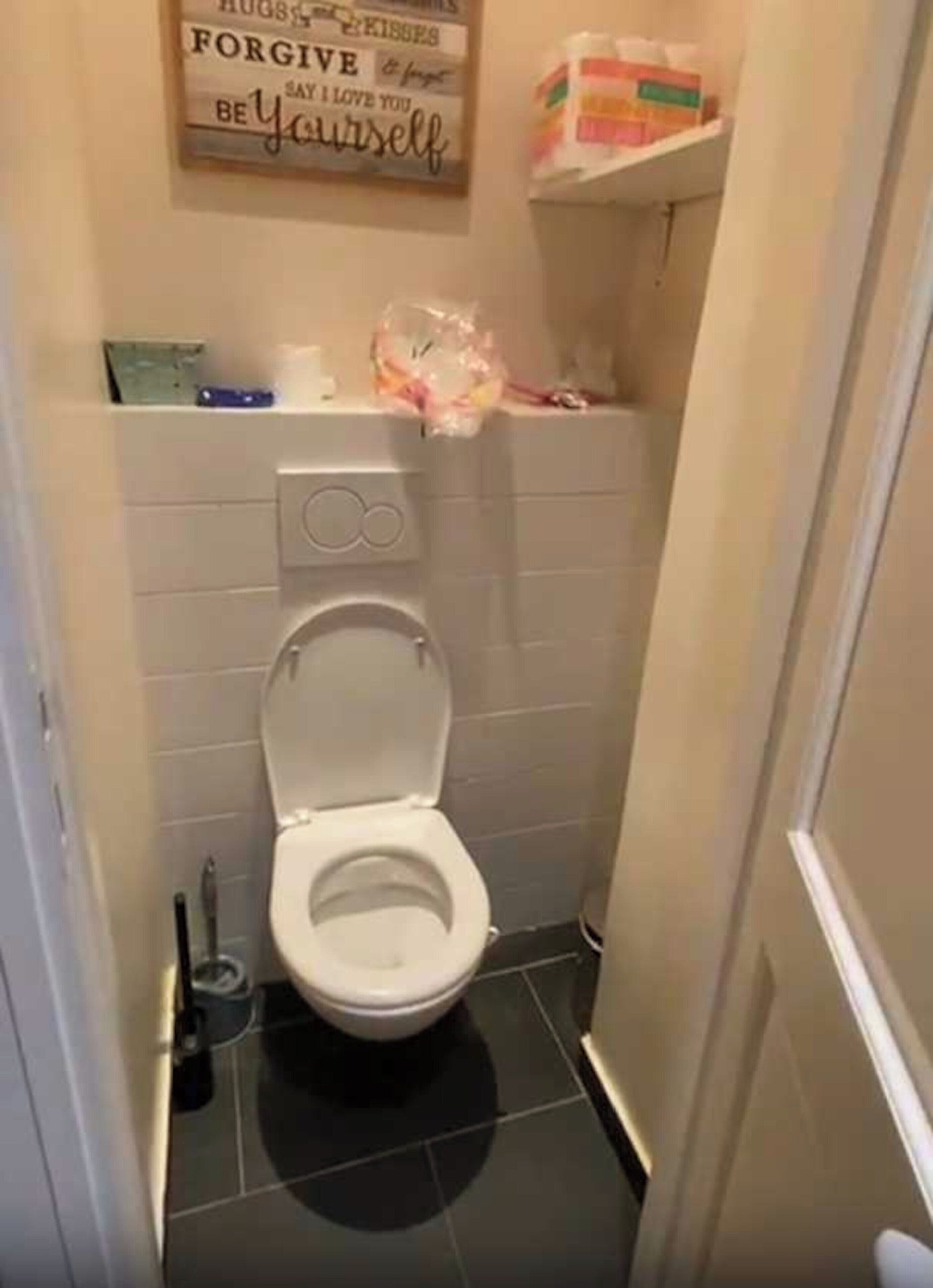 A small bathroom with a toilet, a trash bin, and a wall-mounted sign.